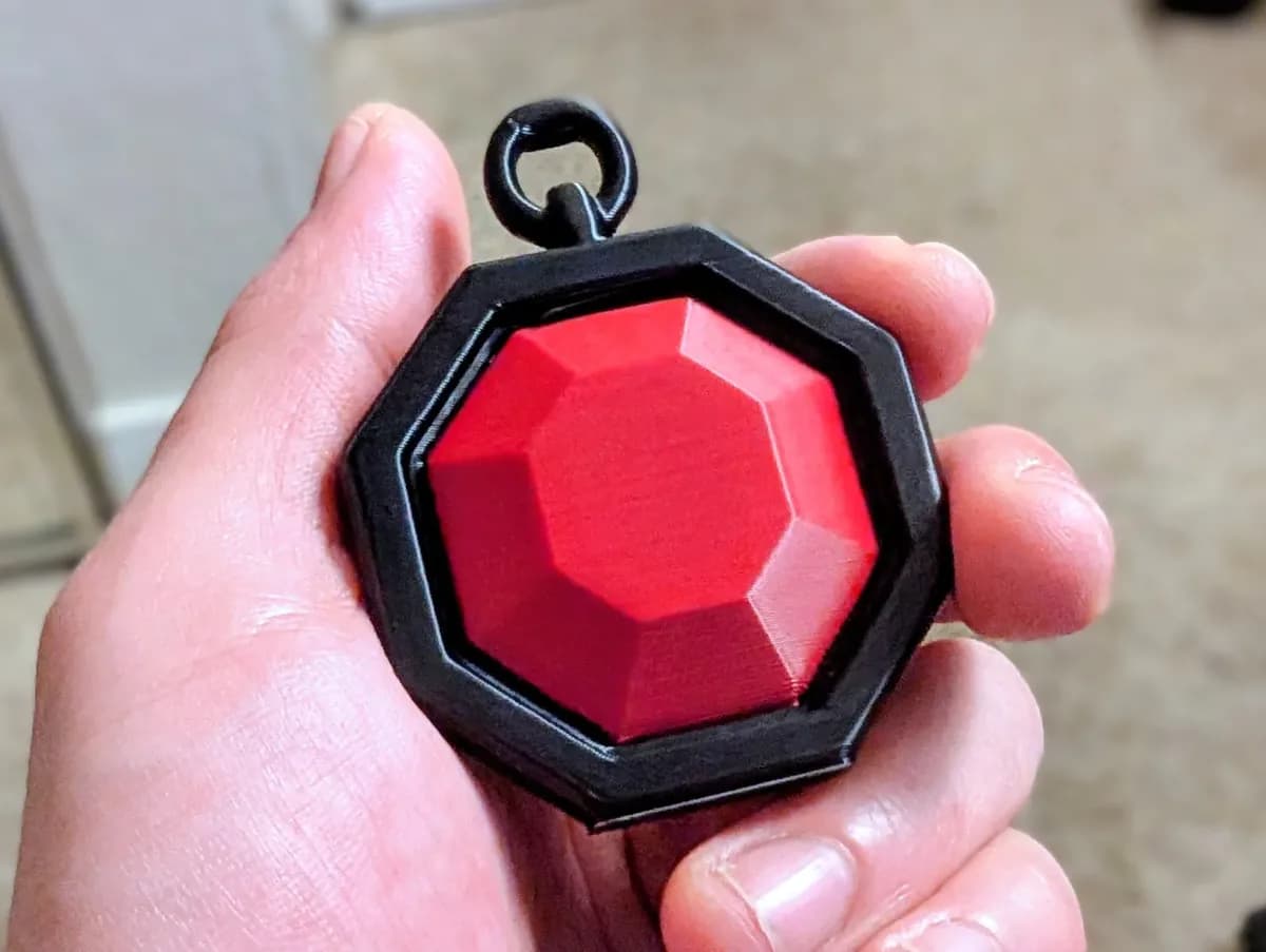 Hanger in edelsteenvorm in een hand: achthoekig zwart frame met een geslepen rode steen en een oogje bovenaan