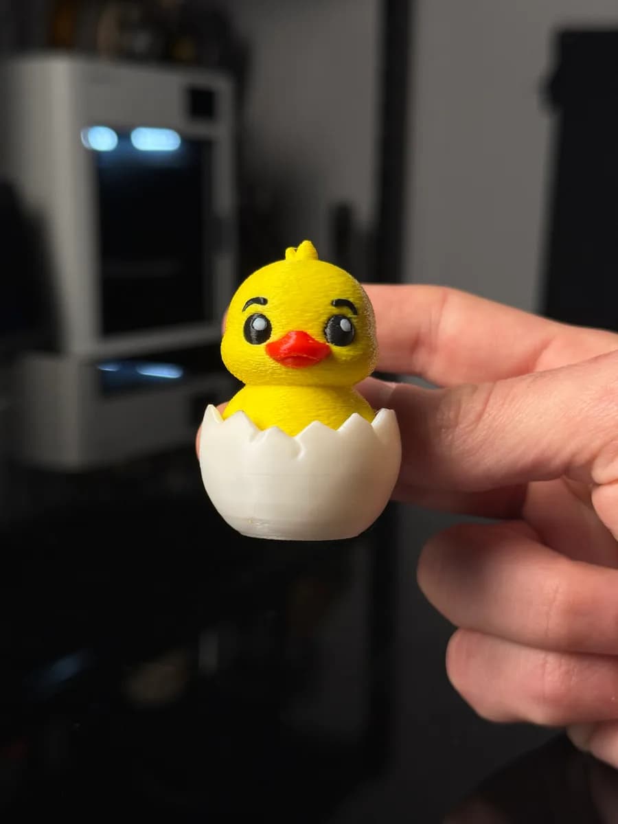 Eend sleutelhanger in een hand: geel eendje met oranje snavel en zwarte oogjes in een witte eierschaal