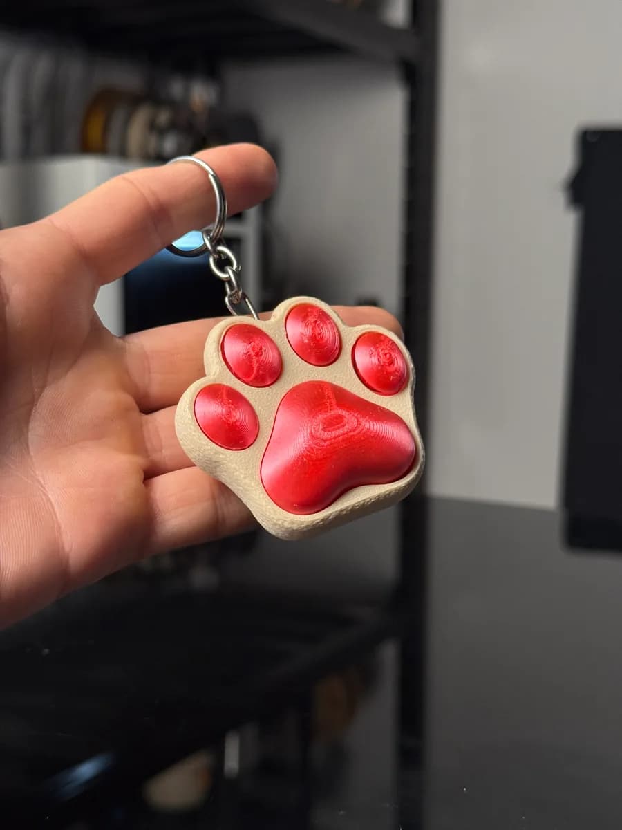 Kattenpootje sleutelhanger in een hand: crème pootje met rood kussentje en vier rode teenboontjes, aan een metalen sleutelring