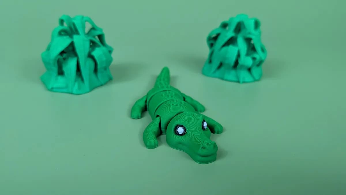 Beweegbare krokodil-sleutelhanger van voren: felgroene krokodil met witte ogen en zwarte pupillen, tussen twee geprinte plantjes
