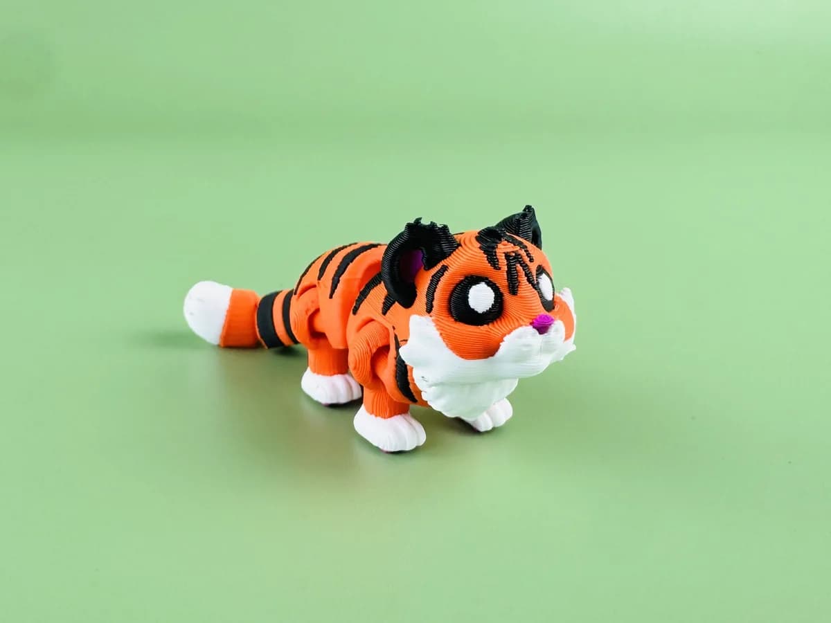 Beweegbare tijger-sleutelhanger, oranje met zwarte strepen en een witte snuit, op een groene achtergrond