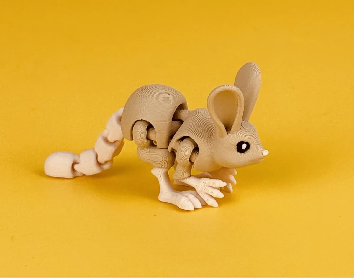 Beweegbare springmuis-sleutelhanger, grijsbeige met grote oren en lichte achterpoten, op een gele achtergrond