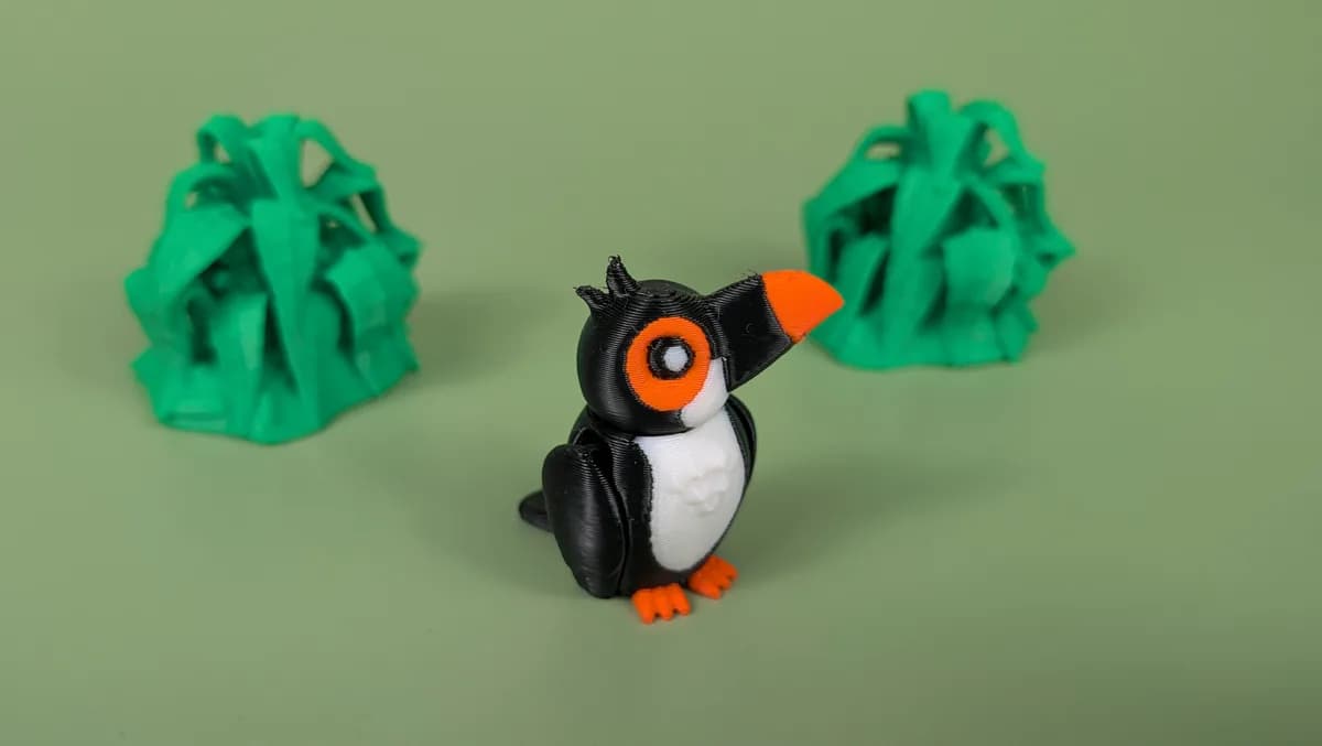 Beweegbare toekan-sleutelhanger: zwarte toekan met witte borst, oranje snavel en oranje oogring, op een groene achtergrond