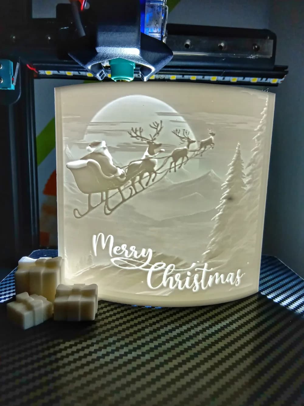 Verlichte gebogen kerst-lithophane waarop een slee en winterlandschap zichtbaar worden.