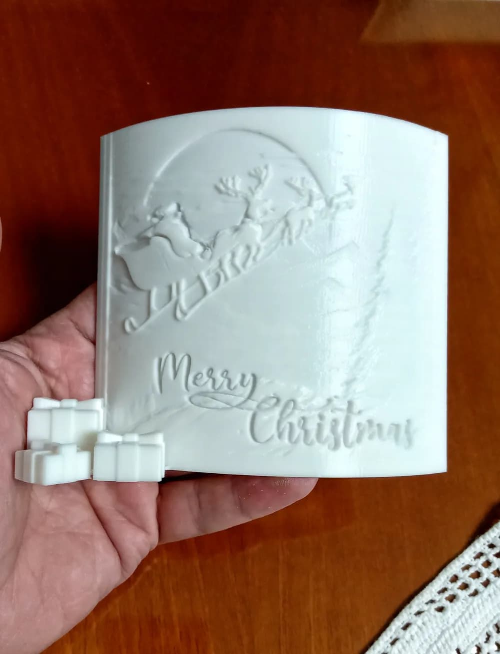 Witte gebogen kerst-lithophane zonder tegenlicht, vastgehouden boven een houten tafel.