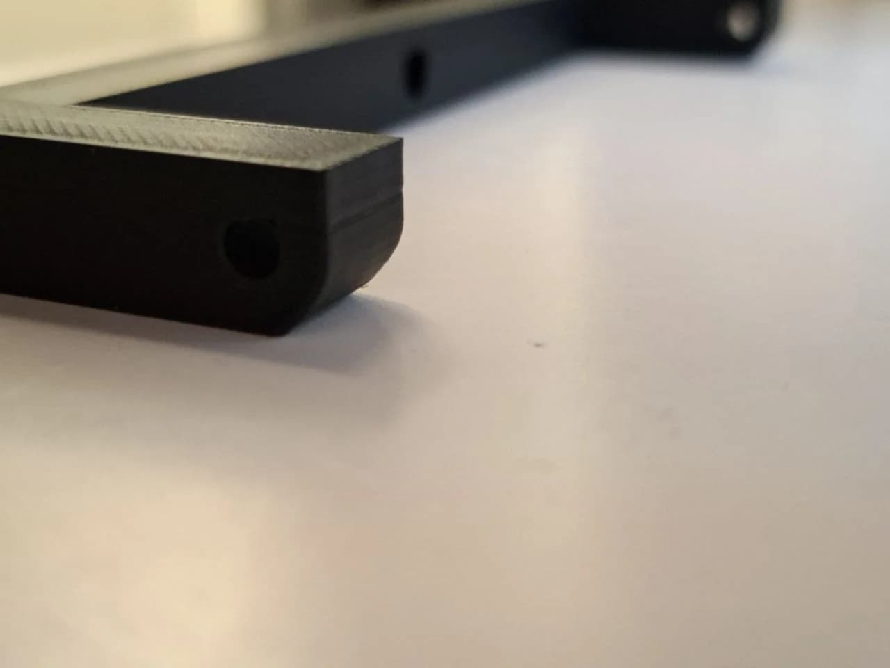 Angled view of the first black PLA+ trial with a rough horizontal hole and uneven edges.