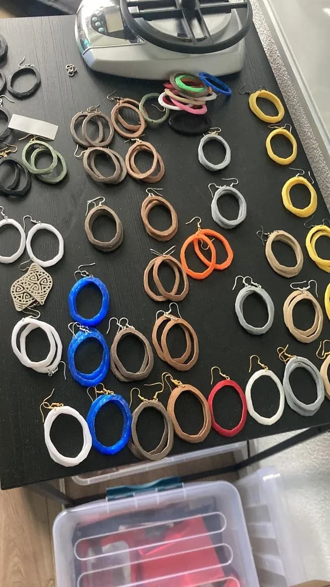 Werktafel met tientallen afgewerkte 3D-geprinte oorbellen in verschillende kleuren en vormen.