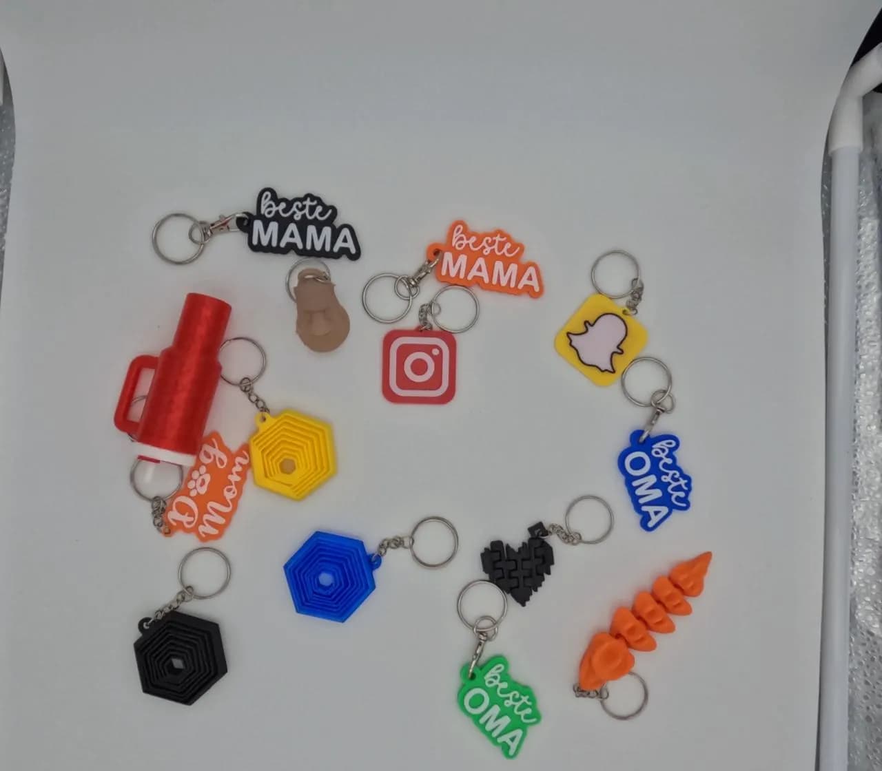 Verschillende 3D-geprinte sleutelhangers in een kring: tekst, iconen, spiralen en figuren.