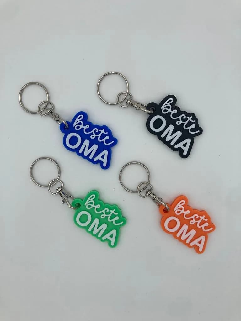 Four 3D-printed keychains reading beste OMA in blue, black, green and orange.