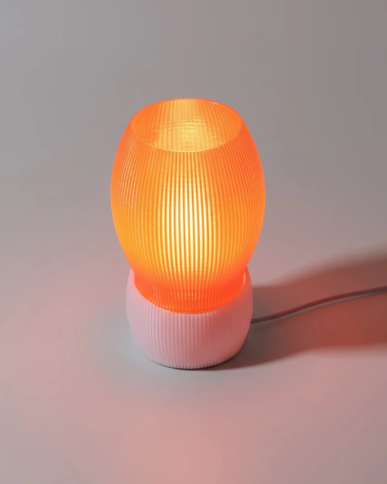 FlowForm Ripple-ontwerpvoorbeeld van Jer{folio}: oranje geribbelde kap op een lage lichte ribbelvoet, met licht aan