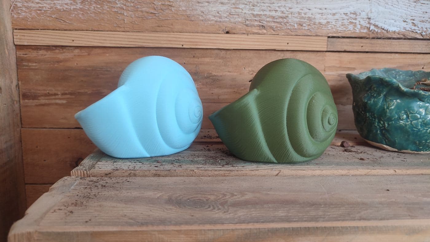 Twee Natica schelpvazen, lichtblauw en olijfgroen, liggend op een houten plank