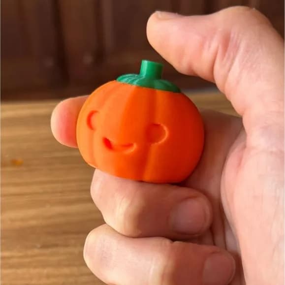 Pompoenclicker – hand houdt een oranje pompoentje met lachend gezicht en groen steeltje