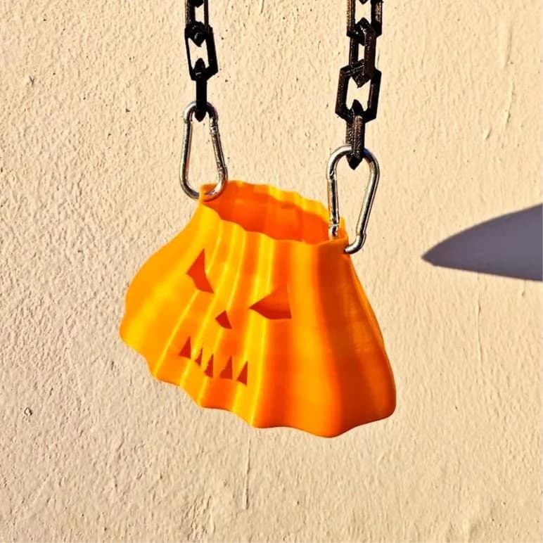 Pompoentasje met ketting – oranje pompoentasje met uitgesneden gezicht aan bruine kettingen tegen een lichte muur